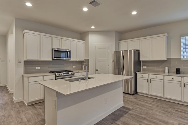 kitchen featuring light stone counters, appliances with stainless steel finishes, an island with sink, and white cabinets