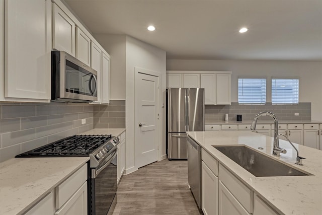 kitchen featuring white cabinetry, sink, light stone counters, light hardwood / wood-style floors, and stainless steel appliances