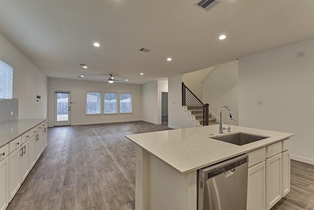 kitchen featuring an island with sink, sink, white cabinets, stainless steel dishwasher, and light stone countertops