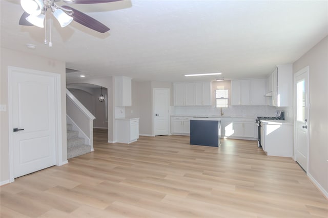 kitchen with white cabinets, light hardwood / wood-style floors, decorative backsplash, and stainless steel gas range oven