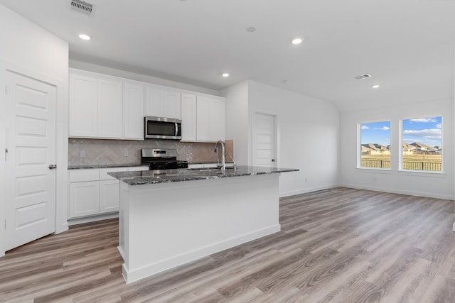 kitchen with white cabinetry, backsplash, a center island with sink, and appliances with stainless steel finishes