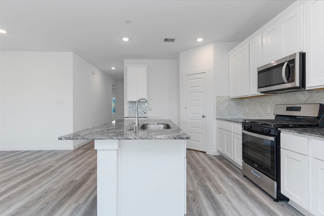 kitchen with a kitchen island with sink, light stone countertops, white cabinetry, and stainless steel appliances