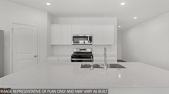 kitchen with light stone countertops, white cabinetry, appliances with stainless steel finishes, and sink