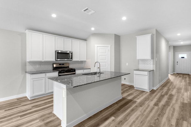 kitchen featuring sink, appliances with stainless steel finishes, white cabinetry, dark stone countertops, and an island with sink