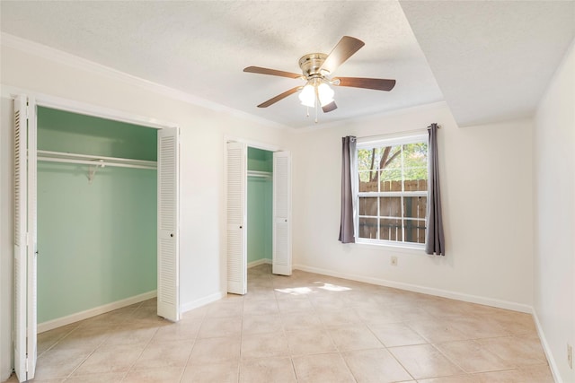 unfurnished bedroom with crown molding, two closets, a textured ceiling, and ceiling fan