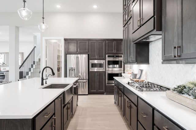 kitchen with backsplash, stainless steel appliances, light hardwood / wood-style floors, an island with sink, and decorative light fixtures