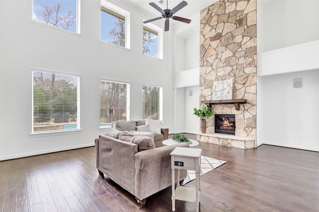 living room with ceiling fan, a towering ceiling, dark hardwood / wood-style floors, ornamental molding, and a stone fireplace