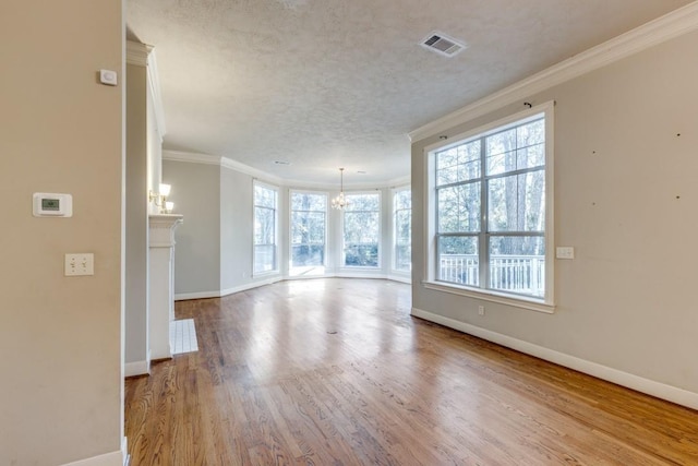 empty room with a notable chandelier, crown molding, a textured ceiling, and light wood-type flooring