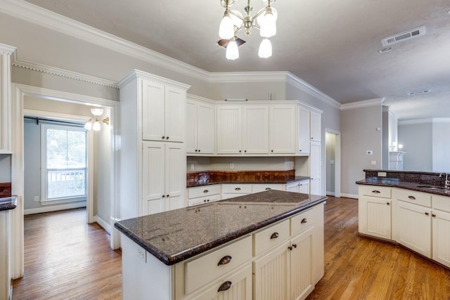 kitchen with pendant lighting, crown molding, a notable chandelier, white cabinets, and light wood-type flooring