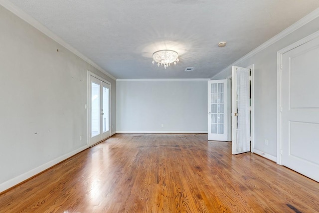 empty room with french doors, ornamental molding, an inviting chandelier, and wood-type flooring