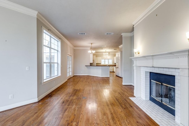 unfurnished living room with ornamental molding, wood-type flooring, a chandelier, and a fireplace