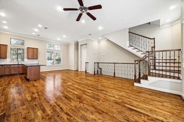 unfurnished living room with sink, dark wood-type flooring, ornamental molding, and ceiling fan