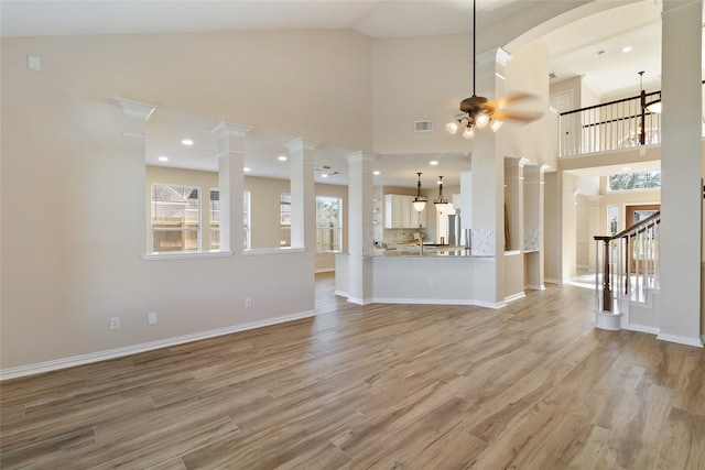 unfurnished living room with ceiling fan, a high ceiling, light hardwood / wood-style flooring, and ornate columns