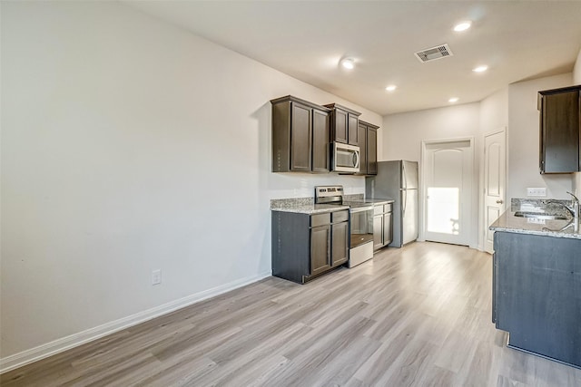 kitchen with dark brown cabinetry, appliances with stainless steel finishes, sink, and light stone counters