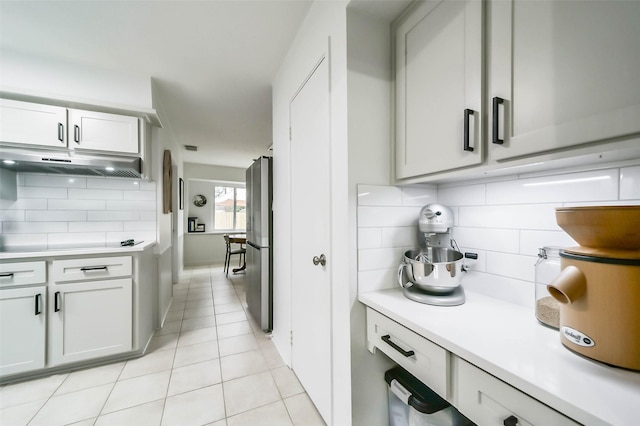 kitchen with light countertops, light tile patterned flooring, freestanding refrigerator, and under cabinet range hood