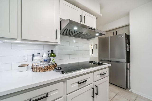 kitchen featuring tasteful backsplash, freestanding refrigerator, black electric cooktop, light countertops, and under cabinet range hood