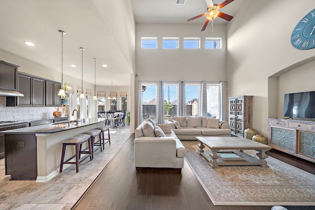 living room featuring ceiling fan, plenty of natural light, light hardwood / wood-style flooring, and a towering ceiling