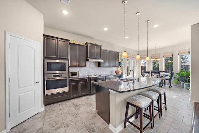 kitchen with sink, a breakfast bar, a kitchen island with sink, hanging light fixtures, and stainless steel appliances