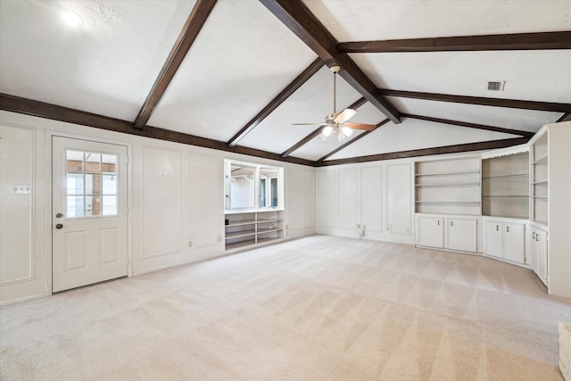 unfurnished living room featuring vaulted ceiling with beams, a wealth of natural light, and light colored carpet