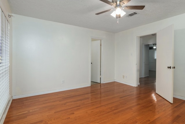 unfurnished room with visible vents, a ceiling fan, a textured ceiling, wood finished floors, and baseboards