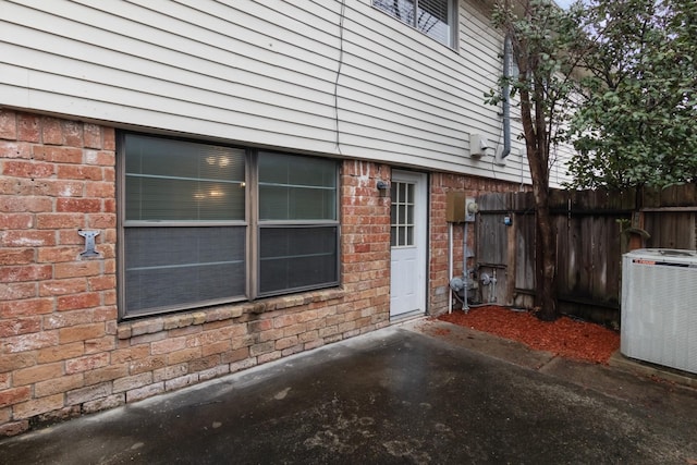 view of home's exterior featuring brick siding, cooling unit, and fence