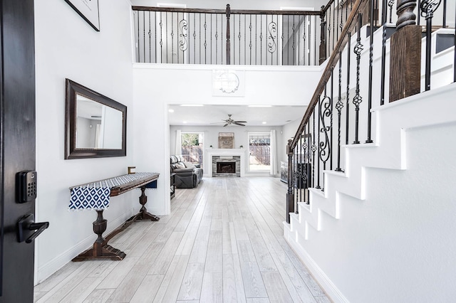 foyer entrance featuring a high ceiling, ceiling fan, a fireplace, and light wood-type flooring