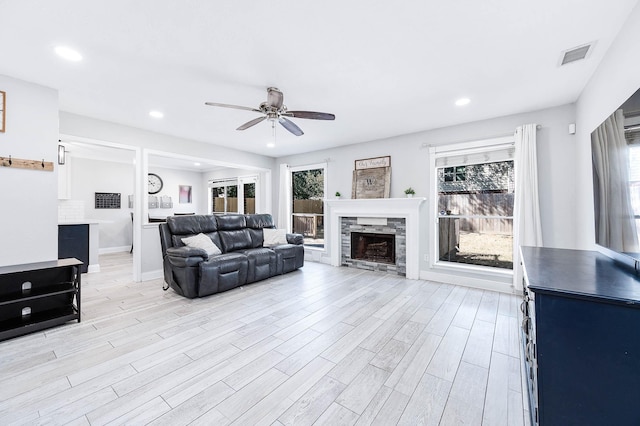 living room featuring a wealth of natural light, a stone fireplace, and light wood-type flooring