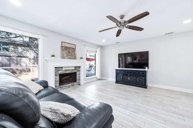 living room with ceiling fan, plenty of natural light, a fireplace, and light hardwood / wood-style flooring