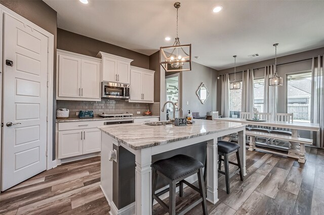 kitchen with white cabinetry, stainless steel appliances, a center island with sink, and pendant lighting