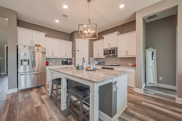 kitchen featuring pendant lighting, white cabinets, a kitchen island with sink, light stone counters, and stainless steel appliances