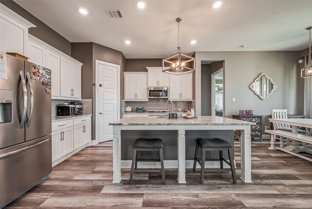 kitchen featuring an island with sink, appliances with stainless steel finishes, pendant lighting, and white cabinets