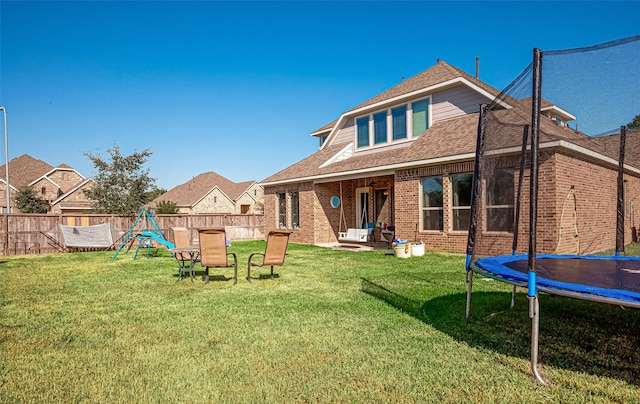 rear view of property with a trampoline, a yard, a patio, and a playground