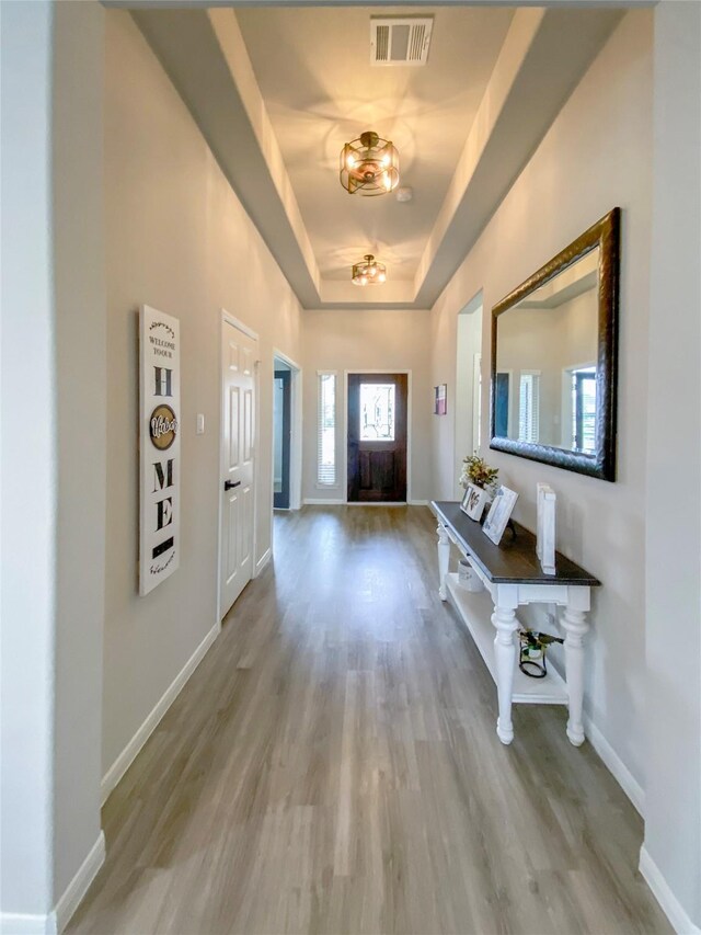 foyer entrance featuring a tray ceiling, visible vents, baseboards, and wood finished floors