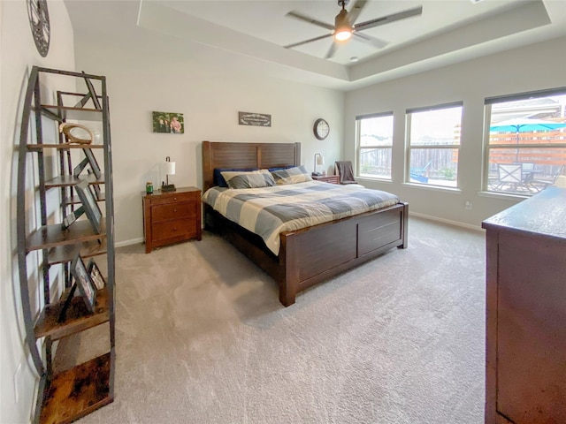 bedroom with light carpet, ceiling fan, a raised ceiling, and baseboards