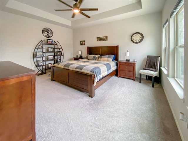 bedroom featuring a ceiling fan, a raised ceiling, light colored carpet, and baseboards