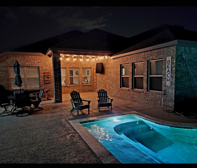 pool at night featuring a patio