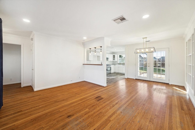 unfurnished living room featuring crown molding, wood-type flooring, french doors, and a notable chandelier