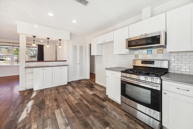 kitchen with dark wood-type flooring, appliances with stainless steel finishes, white cabinetry, hanging light fixtures, and backsplash