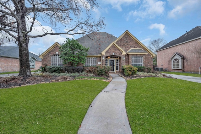 view of front of house featuring a shingled roof, brick siding, and a front lawn