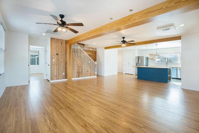 unfurnished living room with wood walls, beamed ceiling, sink, ceiling fan, and light wood-type flooring