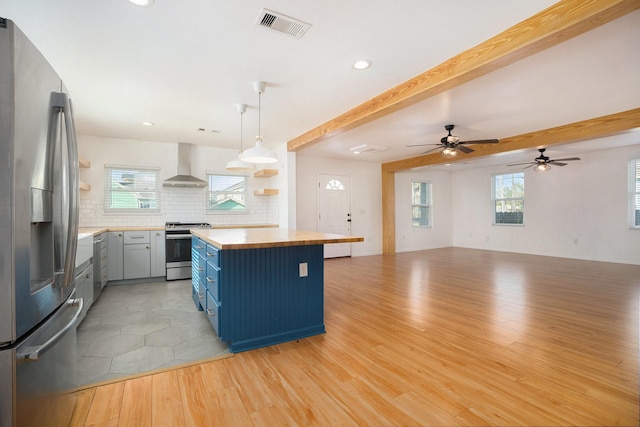 kitchen with appliances with stainless steel finishes, pendant lighting, backsplash, wall chimney range hood, and beam ceiling