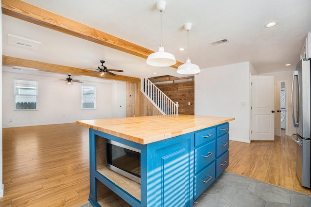 kitchen with stacked washing maching and dryer, stainless steel appliances, blue cabinets, wood counters, and decorative light fixtures