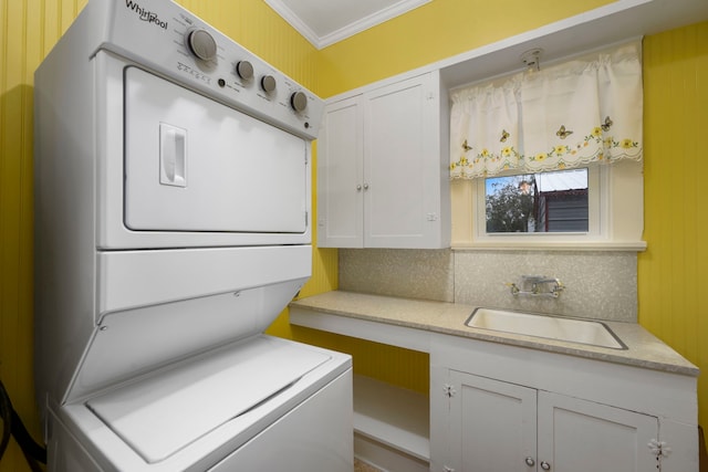 clothes washing area with crown molding, stacked washer and clothes dryer, and sink