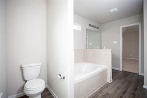 bathroom with a relaxing tiled tub, hardwood / wood-style floors, and toilet