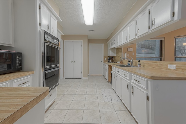 kitchen featuring sink, white cabinets, light tile patterned floors, black appliances, and a textured ceiling