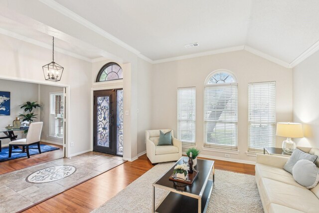 foyer entrance featuring hardwood / wood-style flooring, ornamental molding, vaulted ceiling, and a notable chandelier