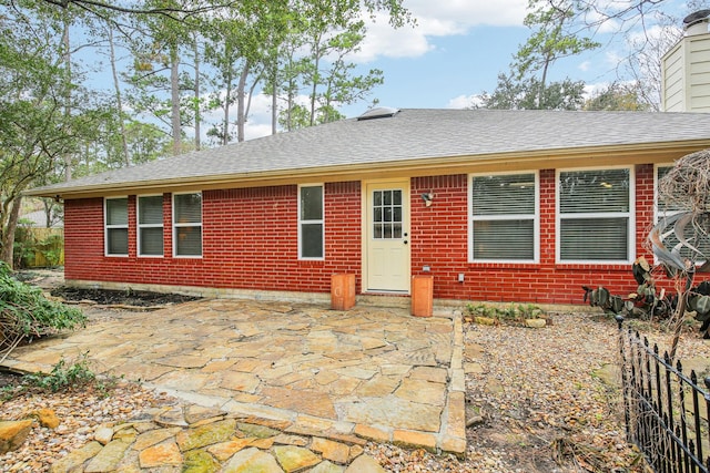 rear view of property featuring a patio, brick siding, roof with shingles, and a chimney