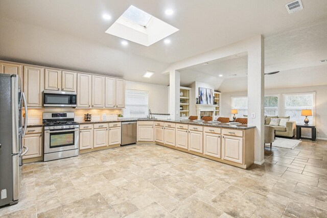 kitchen featuring lofted ceiling with skylight, sink, tasteful backsplash, dark stone countertops, and stainless steel appliances