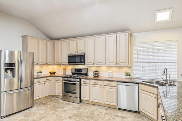 kitchen featuring a sink, stainless steel appliances, dark stone counters, decorative backsplash, and lofted ceiling