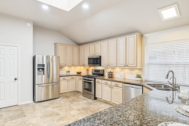 kitchen featuring lofted ceiling with skylight, sink, decorative backsplash, dark stone counters, and stainless steel appliances